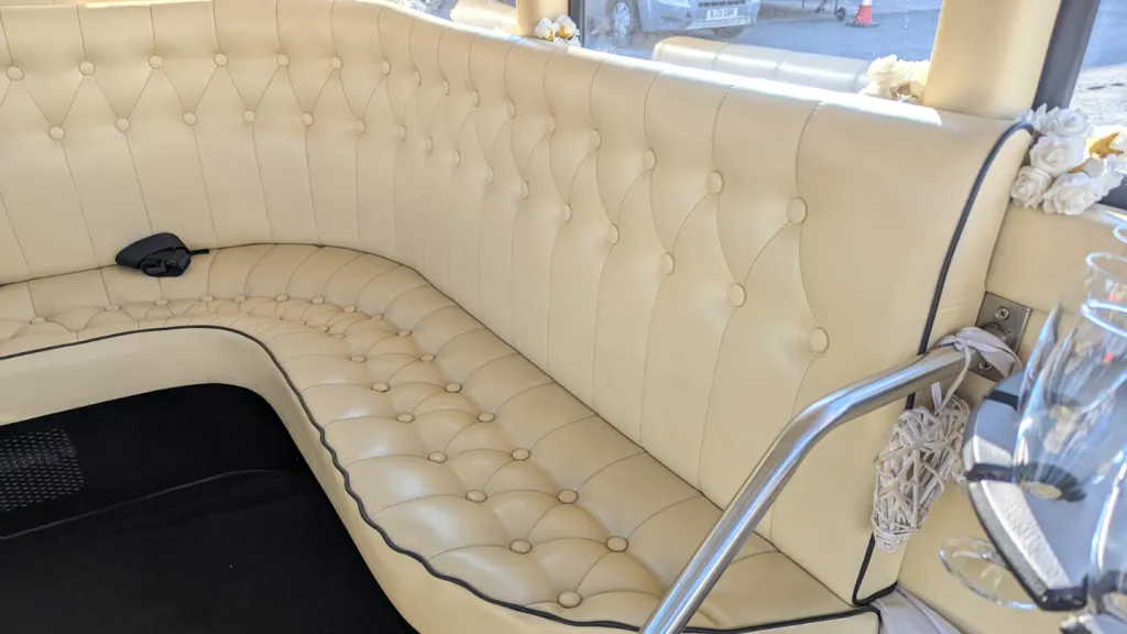 Rear interior view of an Imperial vintage wedding bus with long cream leather bench seating and chrome supports.