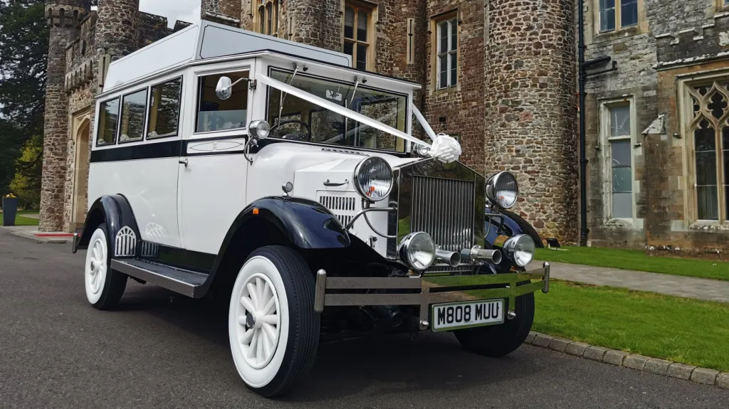Front view of a white Imperial vintage wedding bus with white ribbon tied to the bonnet and shining chrome grille.