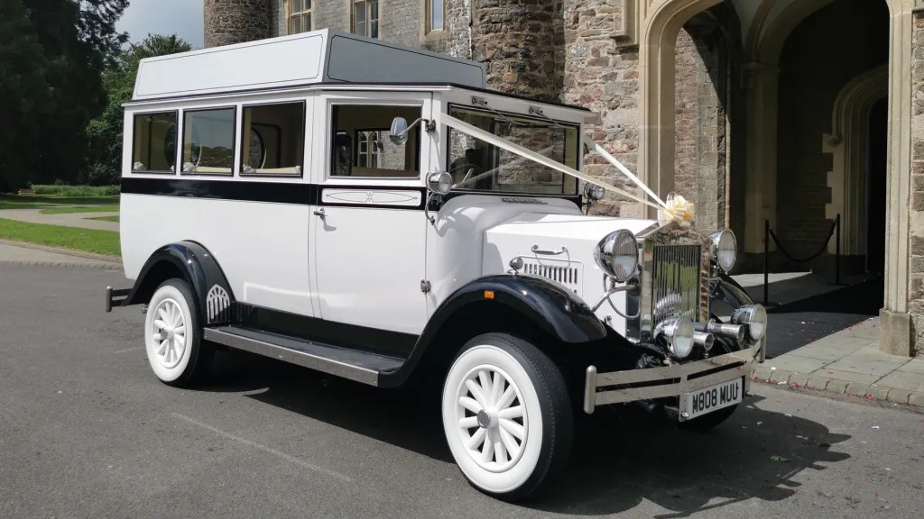 Imperial vintage wedding bus decorated with white ribbons, parked outside a grand stone church entrance.