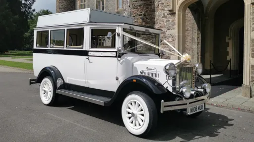 Imperial vintage wedding bus decorated with white ribbons, parked outside a grand stone church entrance.