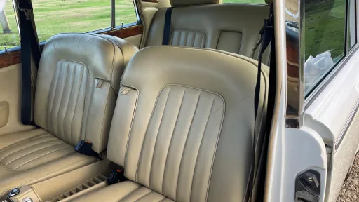 Front interior of a Rolls-Royce Silver Shadow with cream leather seats and polished wooden trim on the doors.
