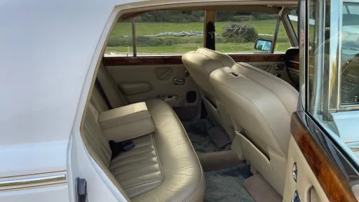 Rear seating inside a Rolls-Royce Silver Shadow featuring plush cream leather upholstery and wooden veneer details.