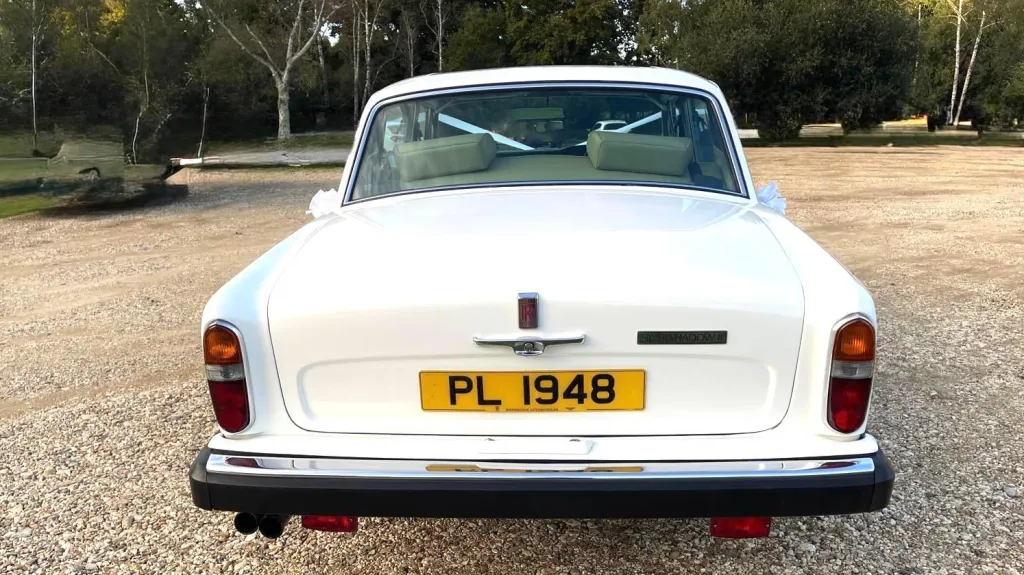Rear view of a white Rolls-Royce Silver Shadow showing chrome bumper, tail lights, and yellow number plate “PL 1948”.
