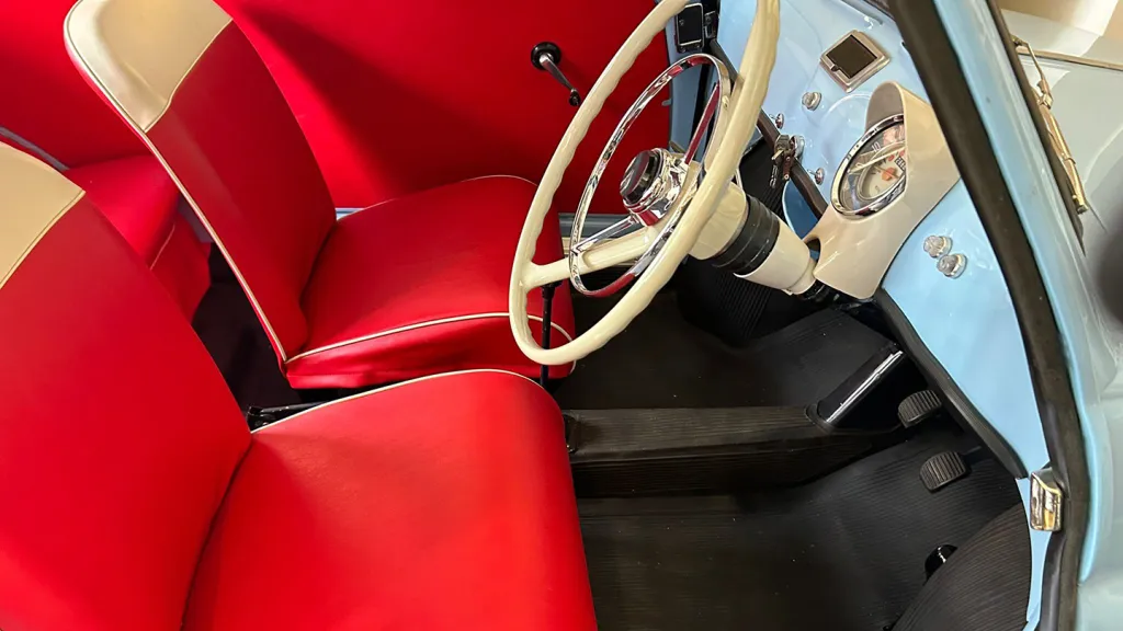Interior of a classic Fiat 500 showing bright red seats with white piping, cream steering wheel and light blue dashboard details.