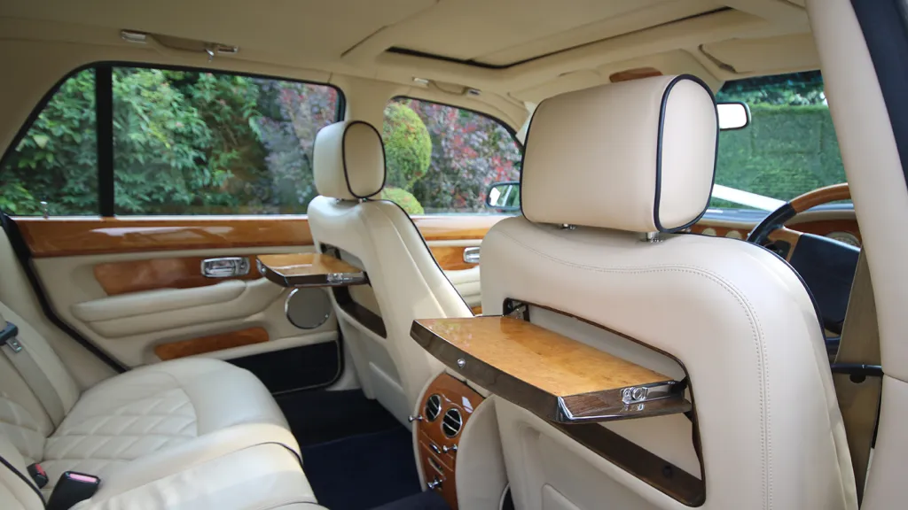Wide rear seating inside a Bentley Arnage with cream quilted leather upholstery and wooden trim.