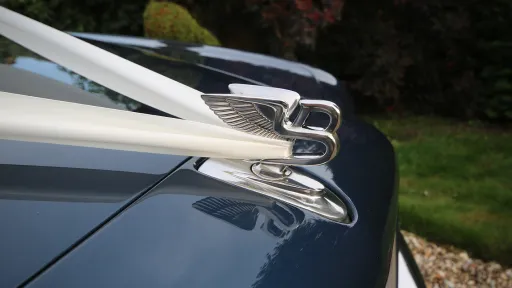 Close-up of the Bentley Flying B bonnet mascot with white wedding ribbons tied across the bonnet.