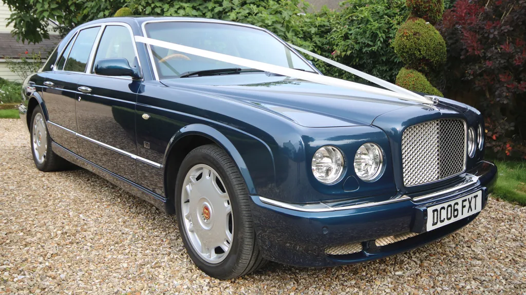 Front angled view of a Bentley Arnage finished in Windsor Blue with chrome grille and alloy wheels, parked on a gravel driveway.
