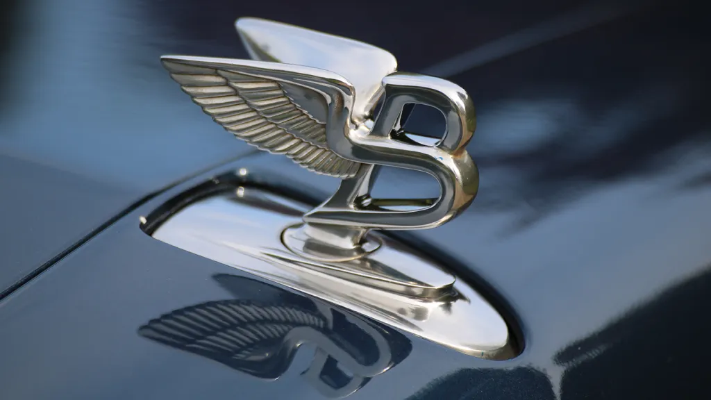 Close-up of the Bentley “Flying B” bonnet mascot on a Windsor Blue Arnage, reflecting the polished paintwork.