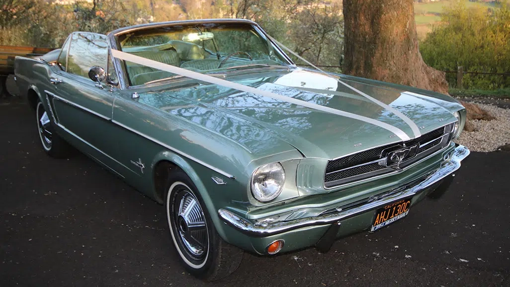 Front view of a classic Ford Mustang convertible decorated with white wedding ribbons tied across the bonnet.