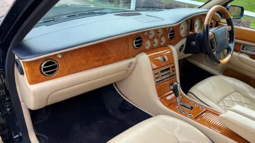 Dashboard view inside a Bentley Arnage with polished wooden fascia, cream leather trim and modern dials.