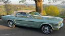 Green classic Ford Mustang convertible with white soft-top roof, parked outdoors on a country road for wedding hire.