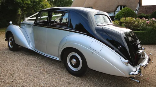 Rear side view of a two-tone 1954 Rolls-Royce Silver Dawn in silver on the side and black roof, showing its elegant curves and chrome bumper.
