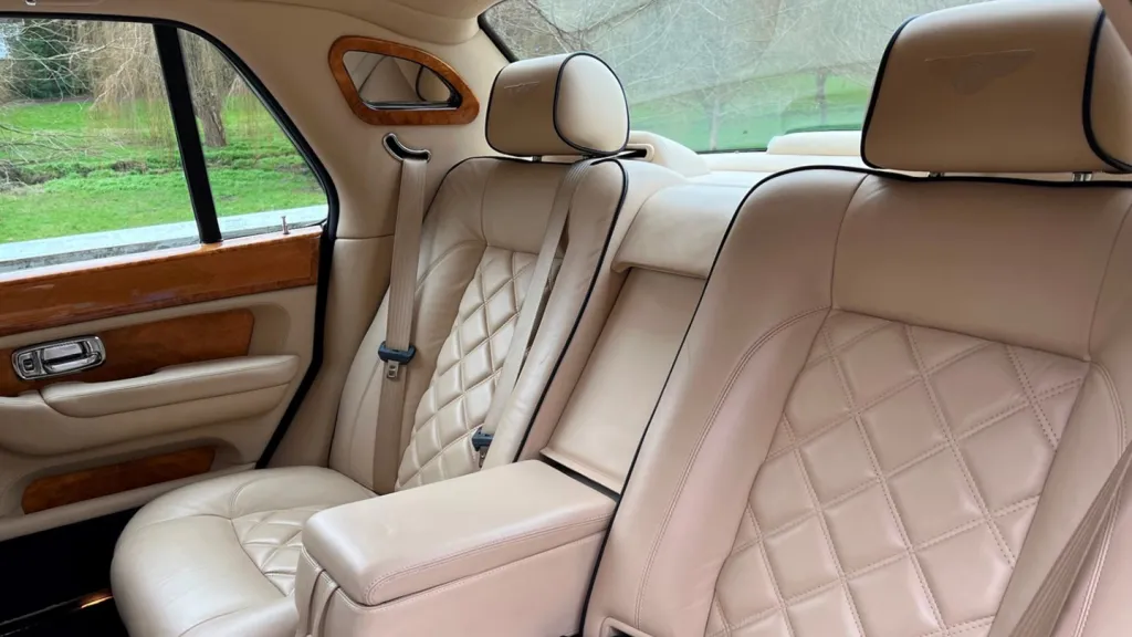 Rear cabin of a Bentley Arnage with cream leather seating, vanity mirror, wooden veneers and spacious legroom.