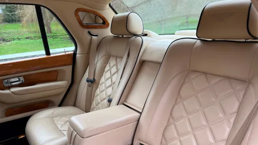 Rear cabin of a Bentley Arnage with cream leather seating, vanity mirror, wooden veneers and spacious legroom.