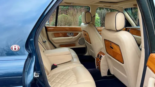 Rear cabin of a Bentley Arnage viewed from the right side, showing plush cream leather seats and fold-down walnut picnic tables.