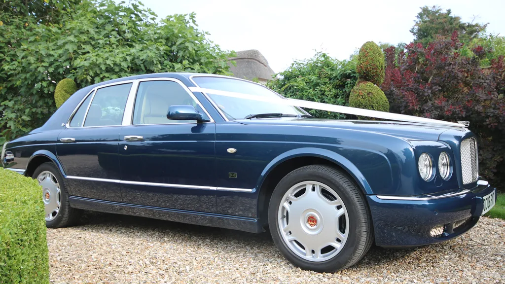 Right side view of a Windsor Blue Bentley Arnage wedding car with chrome accents and alloy wheels, parked on grass in Dorset.