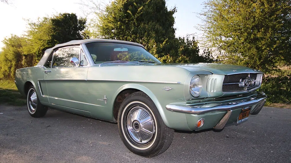 Right side angled view of a vintage Ford Mustang convertible with chrome wheels, parked under trees in Dorset.
