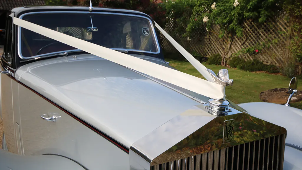 Bonnet view of a 1954 Rolls-Royce Silver Dawn decorated with white wedding ribbons tied to the Spirit of Ecstasy mascot.