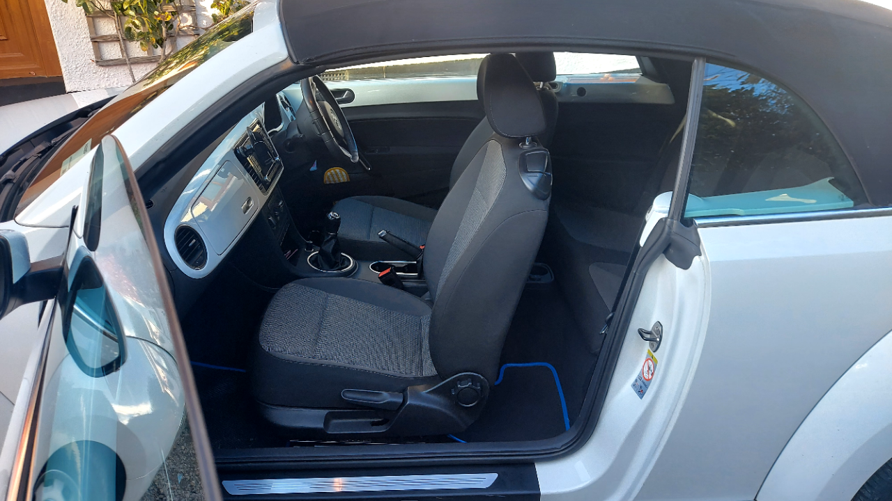 Passenger door open on a modern Beetle showing black interior with black soft top roof close