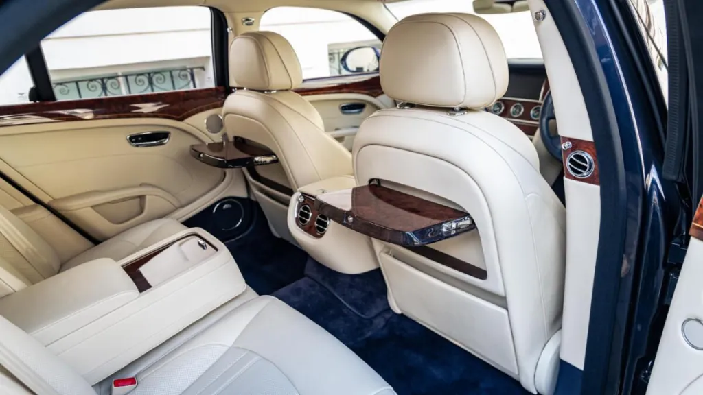 Rear interior seating area with cream leather seats, wooden picnic table open and royal blue carpet