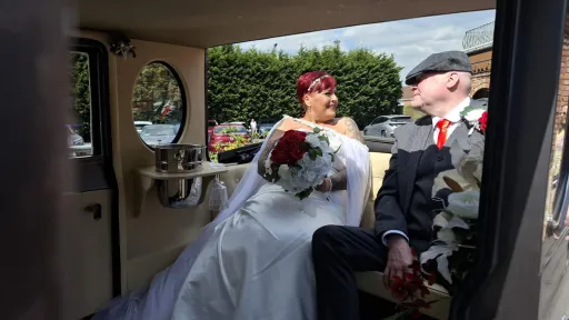 Bride and groom seated inside a silver Imperial vintage wedding car with cream leather interior and polished wood detailing.