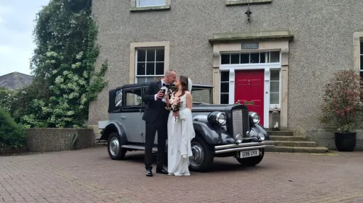 Bride and groom standing next to a silver and black Regent Landaulette wedding car outside a Georgian-style country house.