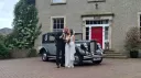 Bride and groom standing next to a silver and black Regent Landaulette wedding car outside a Georgian-style country house.