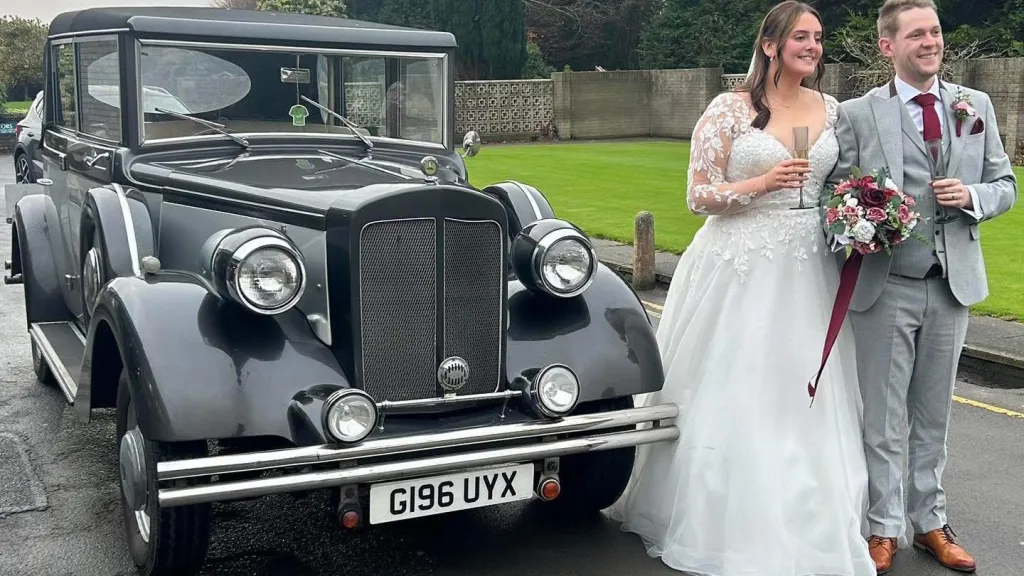 Bride and groom walking away from a vintage silver Regent wedding car decorated with white ribbons, parked on a church driveway in Northern Ireland.