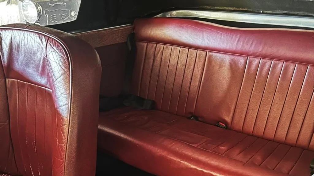Rear interior of a silver Beauford wedding car featuring a classic maroon leather bench seat and vintage wooden trim.