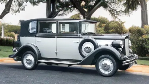 Right side profile of a silver and black Regent Landaulette wedding car with white ribbons and classic chrome details, parked on grass.