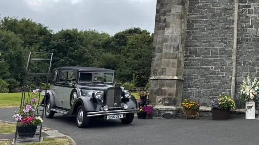 Silver Regent wedding car parked outside a stone church in Ireland, decorated with white ribbons and floral details.