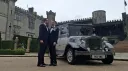 Two grooms standing beside a silver Imperial vintage wedding car outside a castle venue in Northern Ireland.