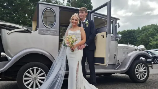 Two-tone silver and grey Imperial wedding car parked outdoors with a bride and groom posing for photos.