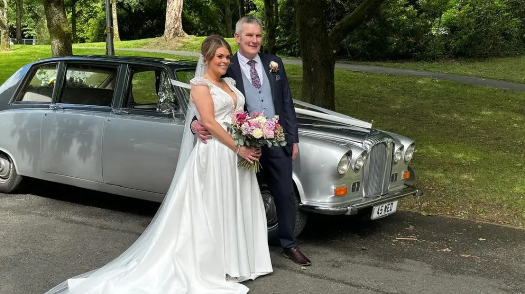Bride and groom standing beside a silver Daimler limousine at a wedding venue in Antrim.