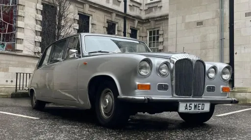 Front view of a silver Daimler DS420 limousine parked outside a grand Belfast building, decorated for a wedding.