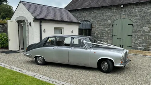 Side view of a silver Daimler limousine with elegant long body and chrome accents, parked outside a countryside venue.