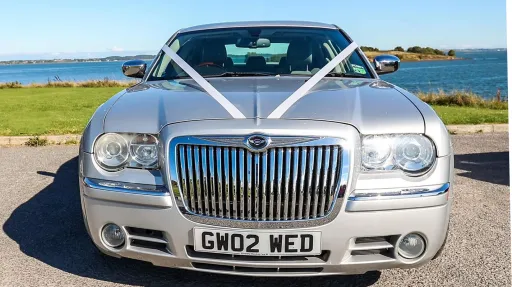 Front view of a silver Chrysler 300C with wedding ribbons on the bonnet, showing its distinctive Bentley-style chrome grille.
