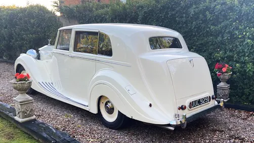 Rear view of a white Rolls-Royce Silver Wraith with sweeping body lines, chrome bumpers, and vintage-style taillights.