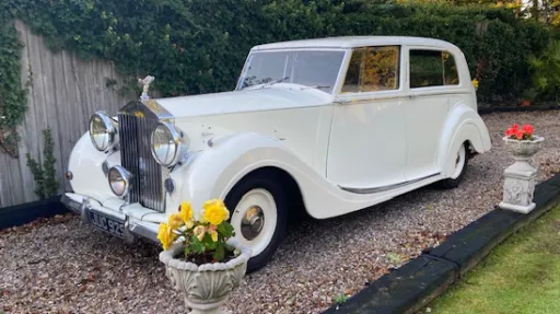 Left side view of a white Rolls-Royce Silver Wraith with gleaming chrome details, parked in a garden setting ready for wedding hire.