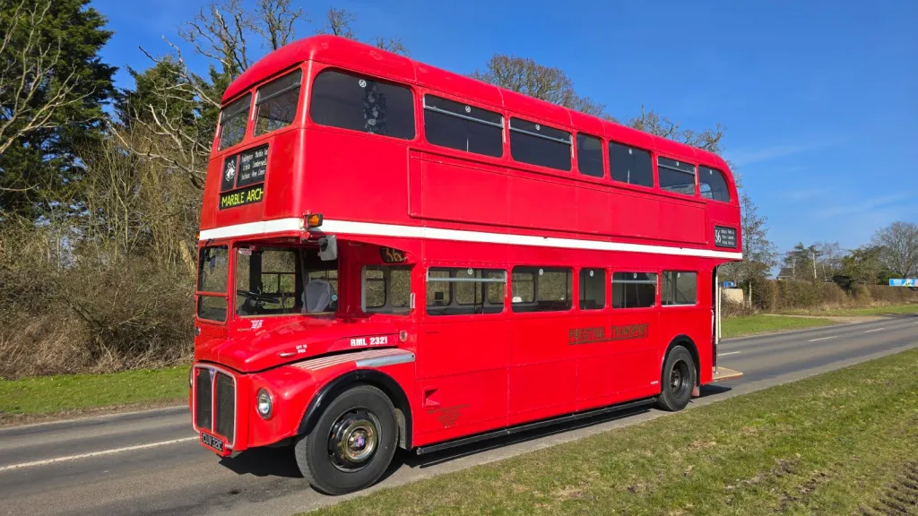 Classic red Routemaster double-decker bus parked on a country lane in Sussex, gleaming in the blue sunshine.