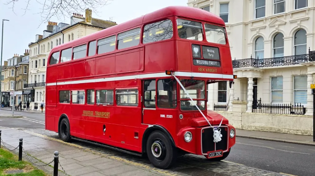 Vintage red Routemaster bus with white wedding ribbons parked outside a countryside venue in Sussex