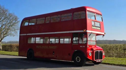 Right side view of a vintage red double-decker Routemaster bus parked in open countryside in Sussex.