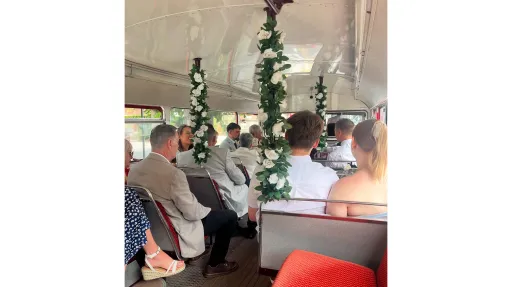 Interior of a vintage red Routemaster bus decorated with floral garlands and ribbons for a wedding journey with passengers seating inside.