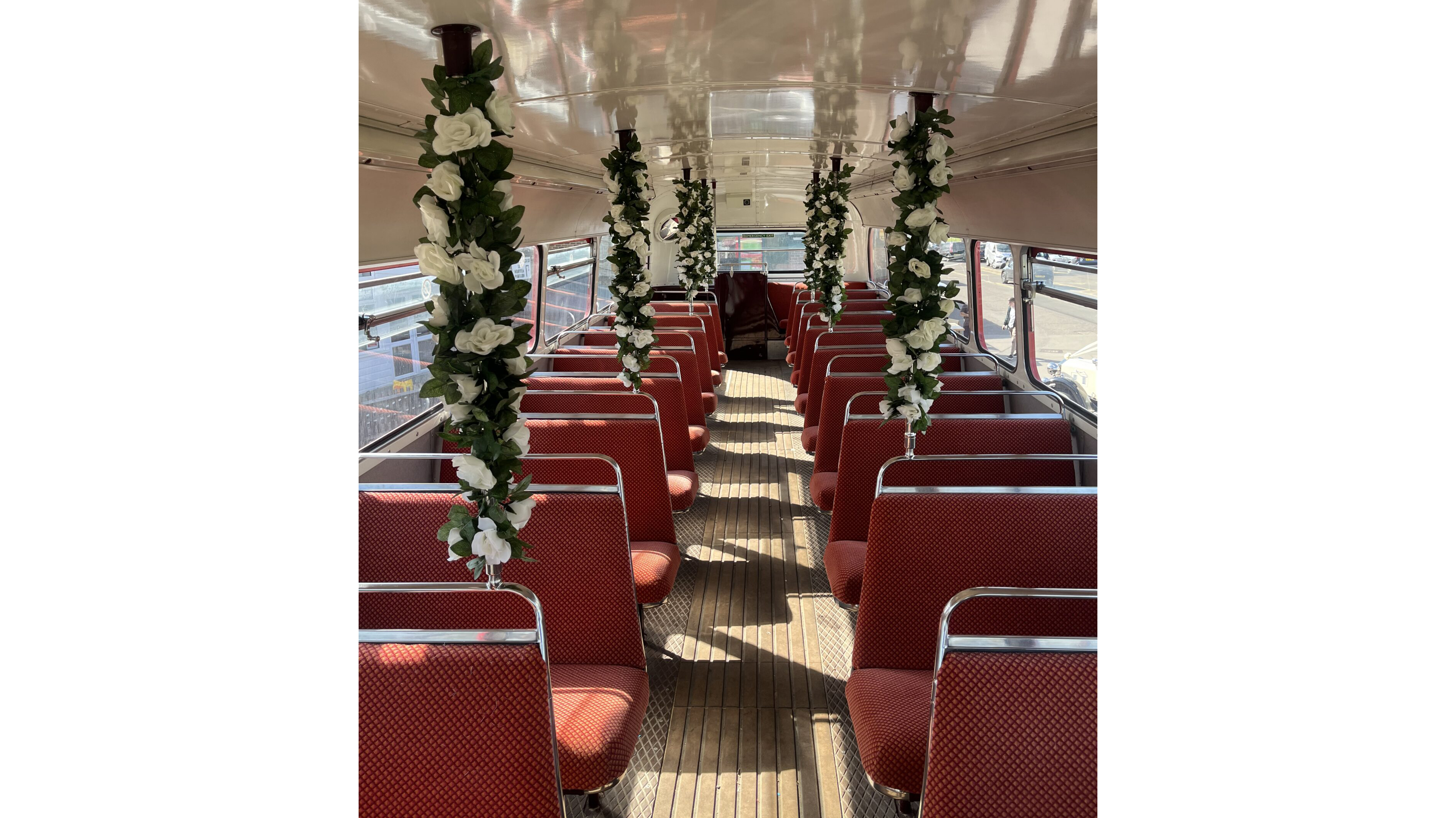 Rows of red patterned seats and floral decorations inside a wedding-themed vintage Routemaster bus.
