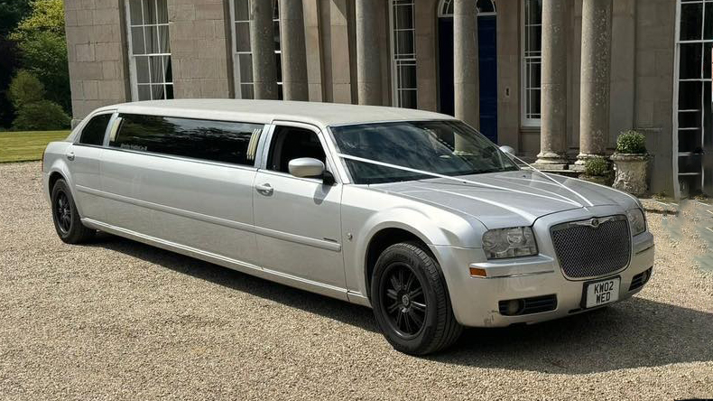 Silver Chrysler stretch limousine with wedding ribbons parked in front of a historic estate venue in Northern Ireland.