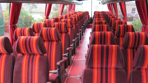Interior of a classic single-decker bus featuring red and orange striped seats arranged in rows with matching curtains.