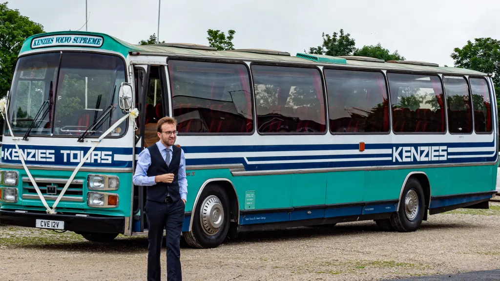 Wedding guests boarding a turquoise single-decker vintage bus outside a stone church, ideal for group wedding transport in Yorkshire.