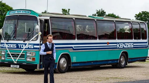 Wedding guests boarding a turquoise single-decker vintage bus outside a stone church, ideal for group wedding transport in Yorkshire.