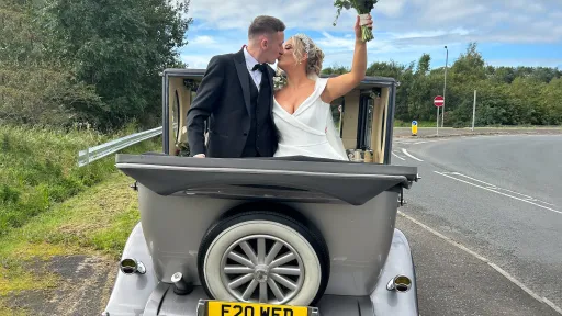Bride and groom sharing a kiss inside a silver vintage Imperial convertible with the roof down on a sunny day.