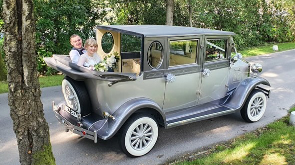 Bride and groom seated inside a silver Imperial vintage convertible wedding car with the roof down, smiling as they travel through Sussex.